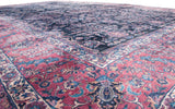 A low angle across the dense pile of a vintage Sarouk, highlighting the rich indigo field and cochineal red border.