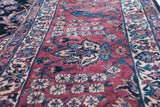 Intricate floral motifs and dense pile on a vintage Sarouk carpet's burgundy field and indigo border.