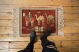 Vintage pictorial Armenian rug with herdsman and camels shown on a floor for scale.