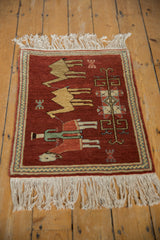 Angled view of a vintage Armenian pictorial rug with a herdsman leading camels across a rust-red field.