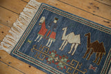 Denim blue pictorial rug detail: herdsman, camels, primitive florals, and ivory fringe.