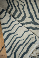 Folded vintage Zebra Kilim rug with ivory and charcoal stripes, hand-woven texture, and fringe.