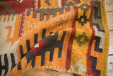 Textured patchwork kilim with orange, brick red, charcoal panels and white cross-hatch stitching.