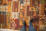 Warm palette patchwork Kilim rug, geometric designs with brick red, saffron, ivory, and prominent cross-stitching.