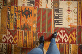 Patchwork Kilim carpet with geometric panels, warm tones, and prominent cross-hatch stitches.