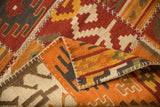 Folded patchwork Kilim shows white cross-stitches, brick red, ivory, and orange geometric patterns.