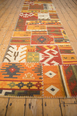 Long angled view of a patchwork kilim runner showcasing repeating geometric panels and raised cross-hatch stitching.