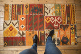 Varied geometric patterns and warm tones on a patchwork kilim rug, highlighting cross-stitch seams.