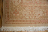 Corner of distressed Indian Soumac carpet, highlighting terra cotta floral patterns and ivory fringe.