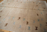 Angled view of the folk art carpet's textured beige field with art silk animal motifs.