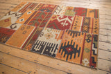 Corner detail of a patchwork Kilim rug with warm geometric patterns and cross-hatch stitching.