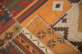 Patchwork kilim panels joined by simulated cross-hatch stitches, displaying geometric guls in warm brick and tangerine tones.