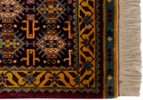 Corner of a vintage rug showing its gold vine border, geometric patterns, and clean ivory fringe.