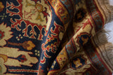 Rolled vintage Kazak rug highlighting rich pile with navy, rust, gold floral design and fringe.