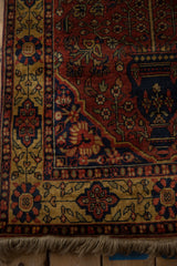 Corner view of a vintage Indian rug with a detailed gold and navy floral border and natural fringe.