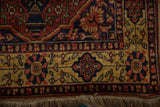 Gold floral border with navy and red motifs shown on the corner of a vintage Indian rug with fringe.