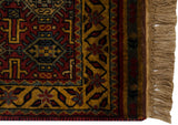 Corner of a vintage rug showing the gold geometric border, wine red details, and natural wool fringe.