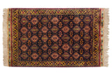 Gold floral vine border and lustrous navy blue pile on the corner of a vintage rug with ivory fringe.
