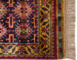 Detail of the vintage rug's corner, highlighting the gold vine border, dense navy blue pile, and natural fringe.