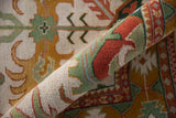 Detail of rolled vintage Indian Caucasian rug, showcasing dense pile, ivory, rust, and seafoam green.