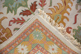Hand-knotted rug corner, revealing geometric foundation and ivory floral pile with fringe.