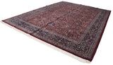 Angled view of a vintage Kashan carpet highlighting its burgundy floral field and wide navy border.
