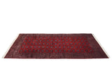 Angled perspective of a vintage Pakistani carpet with a repeating cherry red and navy blue gul pattern.