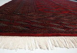 Intricate geometric border and plush red pile of a vintage Turkmen carpet with intact white fringe.