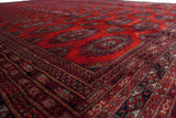Angled view across the plush cherry red pile of a vintage Pakistani carpet, showing the detailed geometric borders.