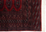 A vintage Pakistani rug's corner shows multiple detailed borders in red and navy beside white fringe.
