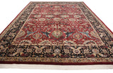 Angled view of a vintage Agra carpet's cherry red field and navy blue lotus flower border.