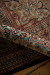 Rolled section of Indian Ardebil rug with plush floral pile in teal, navy, and blush.