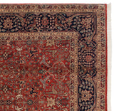 Corner of a vintage Agra rug with a navy vinery border, red selvage, and white fringe.