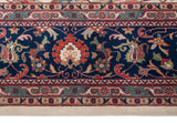 Hand-knotted border detail showing lotus flowers and serrated leaves on a navy blue ground.