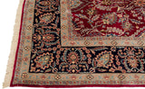 Corner view of a vintage Kerman carpet showing its navy border with palmette details and cream fringe.