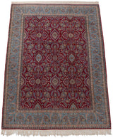 A vintage Kerman carpet featuring a dense cherry red floral field and a wide sky blue border.
