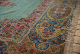 Detailed view of the vintage Kerman carpet's elaborate cameo border and lush ocean green pile.
