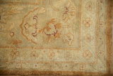 Corner of a vintage Indian Oushak rug with soft gold, copper, and pale green floral patterns.