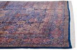 Angled view across the vintage carpet's floral field, showing the corner spandrel and indigo blue border.