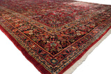 Plush cherry red pile and intricate navy floral border seen on a vintage Sarouk carpet corner.