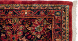 Immaculate corner of a vintage Sarouk carpet showing the plush red and navy pile and clean ivory fringe.