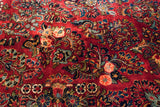 Angled view of intricate floral sprays on the plush, cherry red pile of a Sarouk carpet.