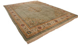 Corner detail of sage green Peking rug with ornate pale gold vines, floral motifs, and fringe.