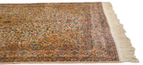 Angled corner view of a vintage carpet's plush pile, floral border, and ivory fringe.
