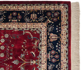 The ornate navy floral border, cherry red field, and clean ivory fringe on a fine Indian carpet.