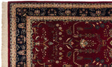 Corner of an Indian Sarouk carpet with an ornate navy floral border and a classic black cherry red field.