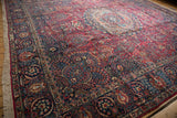 A vintage Tabriz carpet from an angled view, highlighting the intricate red field and navy blue border.
