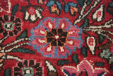 Macro detail of a finely knotted floral motif in raspberry and sapphire blue on a vintage Persian rug.
