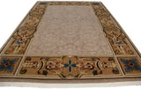 Angled perspective of an Indian carpet with a tone-on-tone beige floral field and an ornate scrolling border.