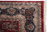 Corner of Indian Sarouk design rug; deep red border, beige cartouche, navy floral field, fringe.
